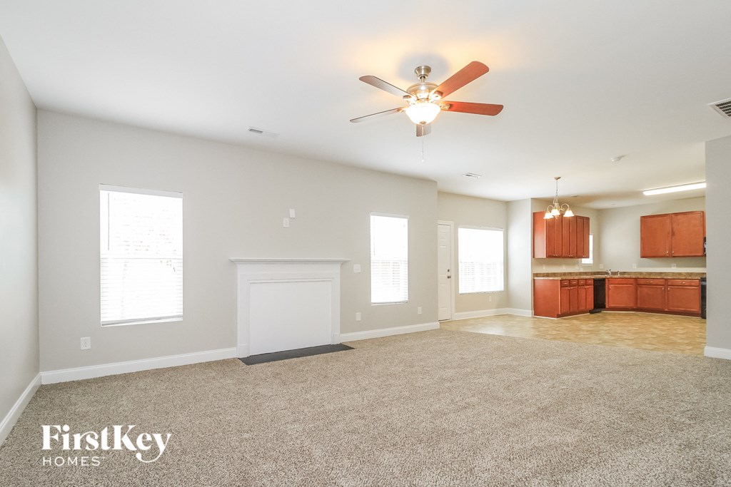 an empty living room with a ceiling fan and a kitchen