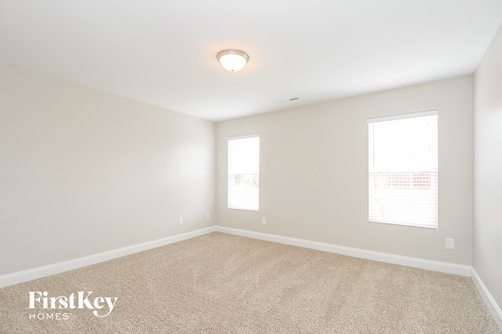 a spacious living room with carpet and two windows