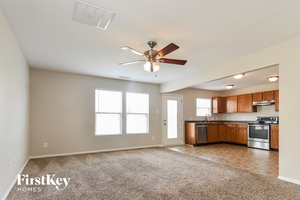 an empty living room with a ceiling fan and a kitchen