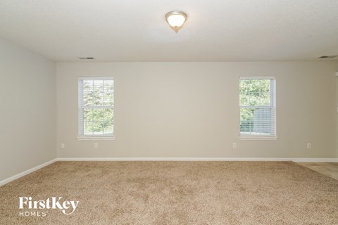 A room with a carpeted floor and two windows.