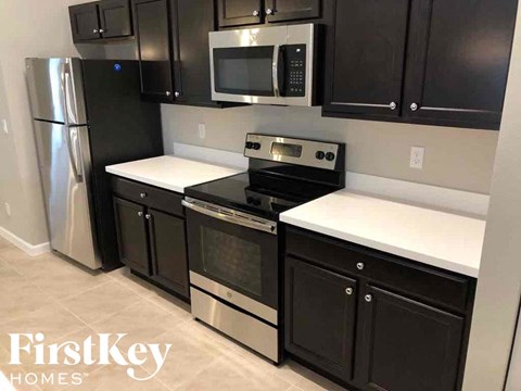 A kitchen with black cabinets and a stainless steel refrigerator.