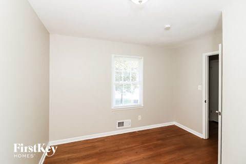 a bedroom with white walls and a window and wood floors
