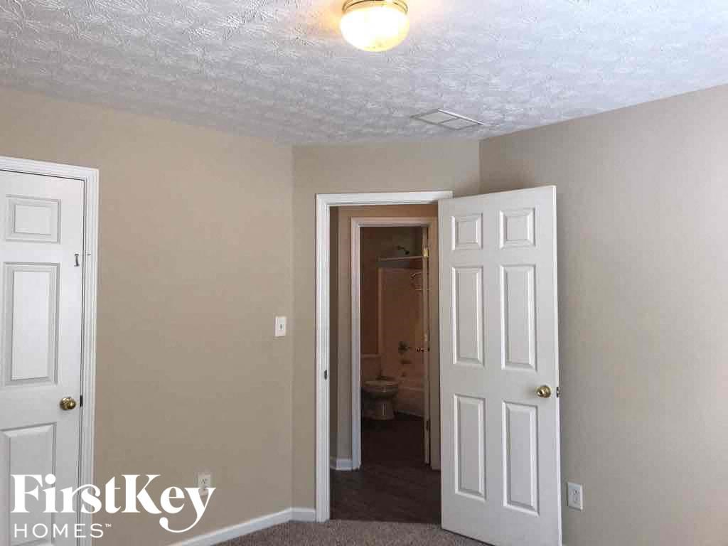 an empty bedroom with a white door and a hallway to a bathroom
