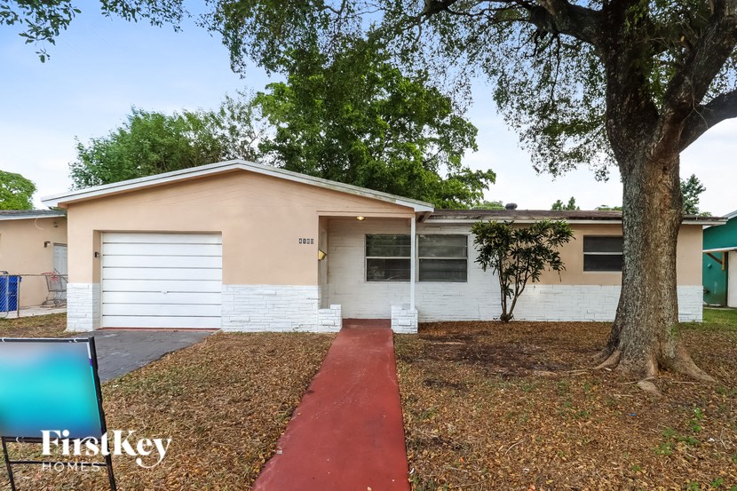 a small white house with a red walkway and a tree