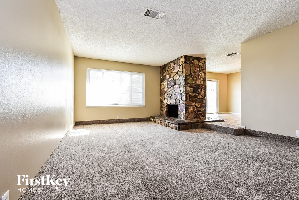 A spacious living room with a stone fireplace and a carpeted floor.