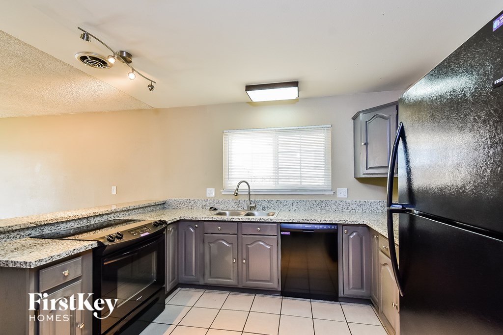 A kitchen with a black refrigerator and a window with blinds.