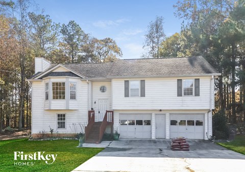 A white house with a garage is surrounded by trees.