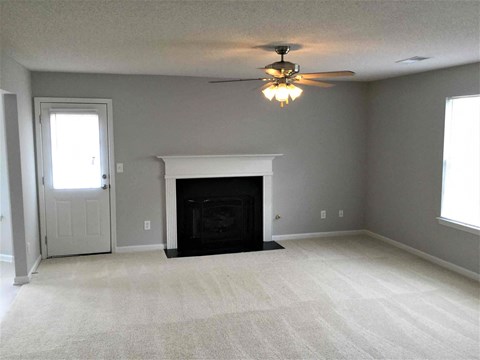 an empty living room with a fireplace and a ceiling fan