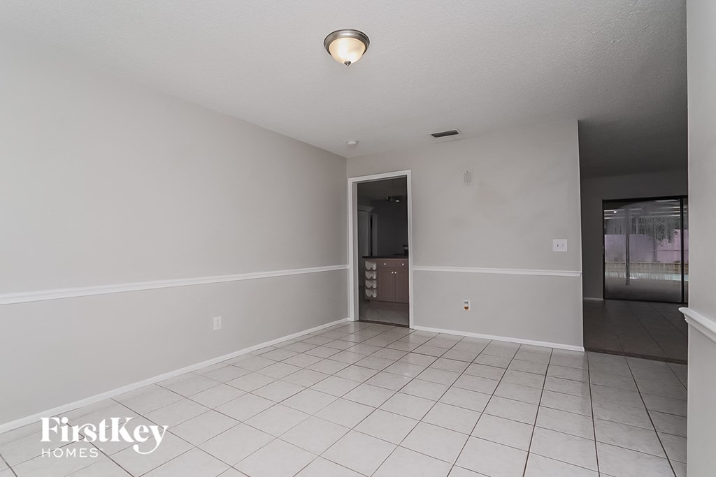 a empty living room with a white tile floor and a door to the kitchen
