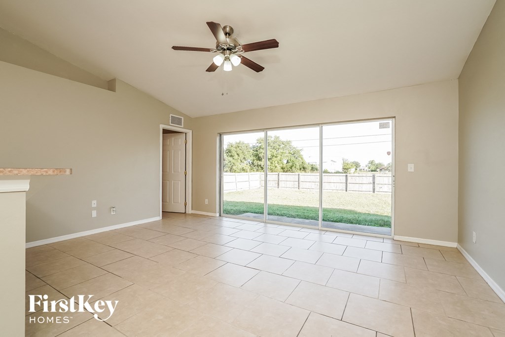 A spacious room with a ceiling fan and sliding glass doors leading to a backyard.