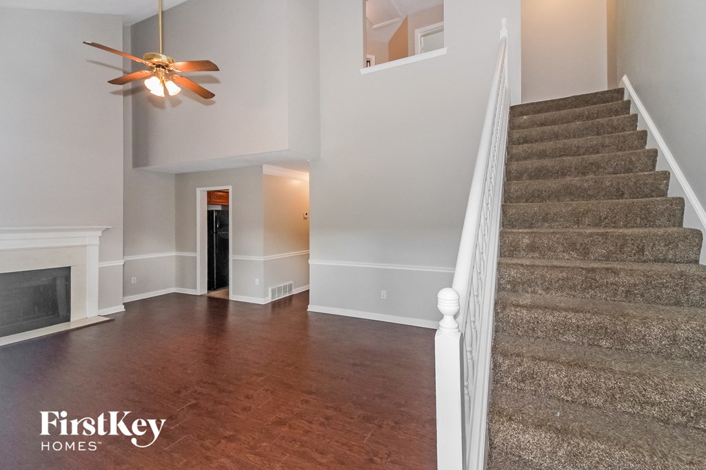 A staircase with a carpeted runner leads up to a landing with a ceiling fan and a fireplace.