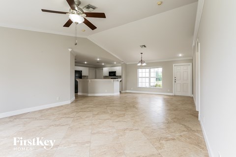 A spacious room with a fan and a kitchen in the background.