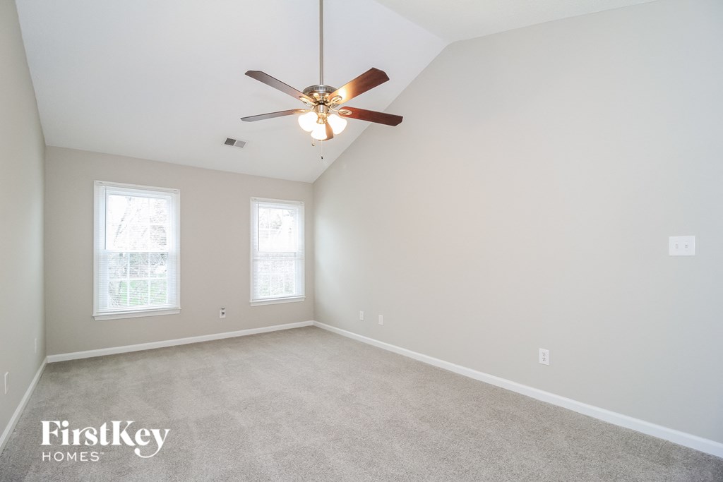 A spacious room with a ceiling fan and two windows.