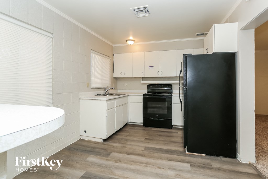 A kitchen with a black fridge, white cabinets, and a wooden floor.