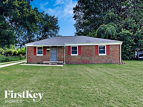 A brick house with a porch and a tree in the background.