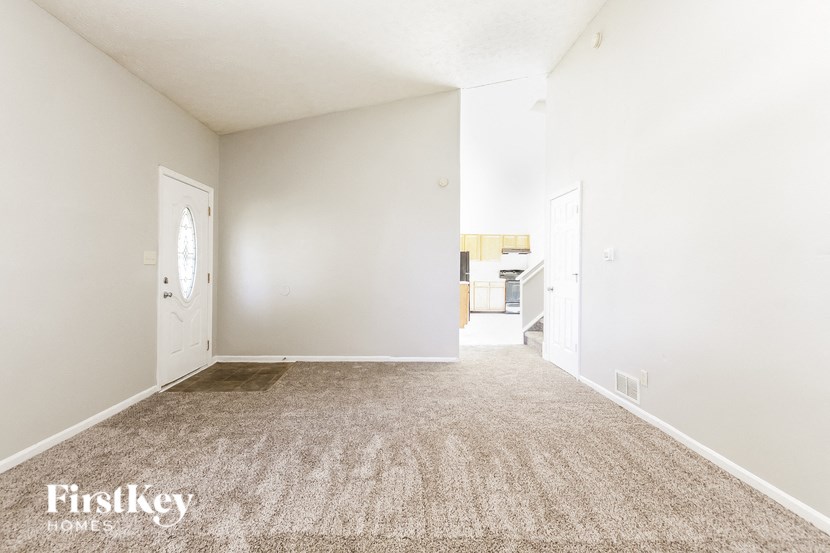 an empty room with a carpeted floor and a door to a kitchen