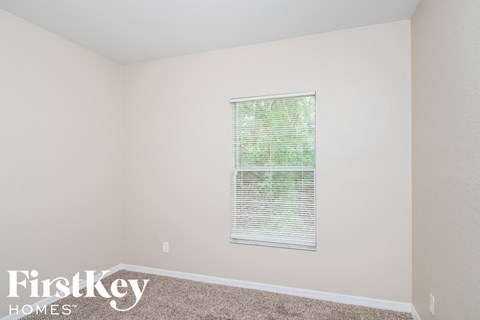 a bedroom with beige carpet and a window with blinds
