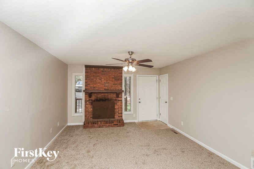 an empty living room with a brick fireplace and a ceiling fan