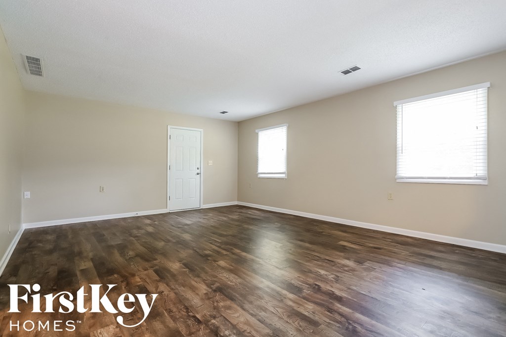 A room with wooden flooring and two windows.