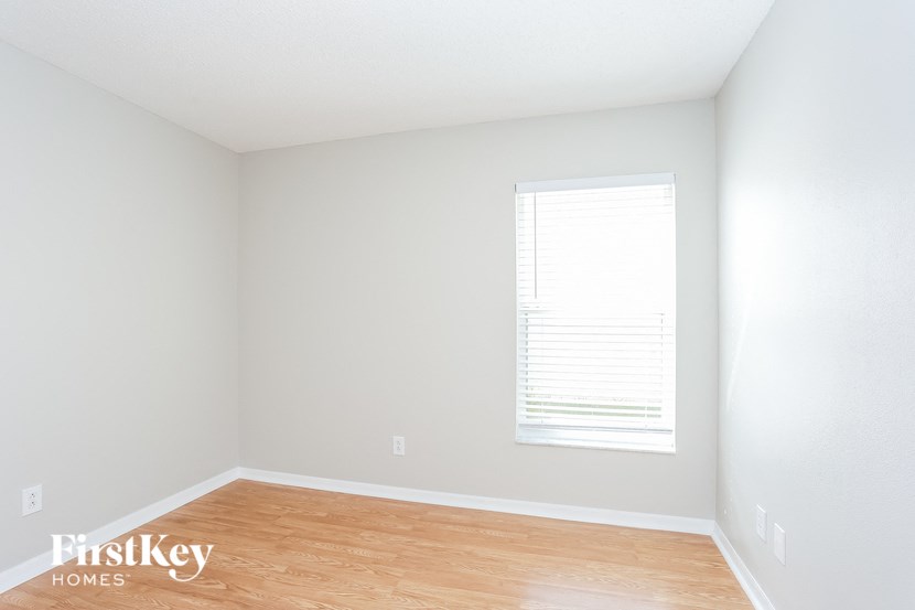 a bedroom with white walls and wood floors and a window