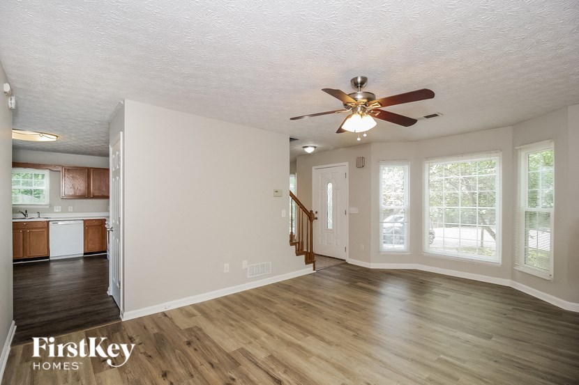 an empty living room with a ceiling fan and a kitchen