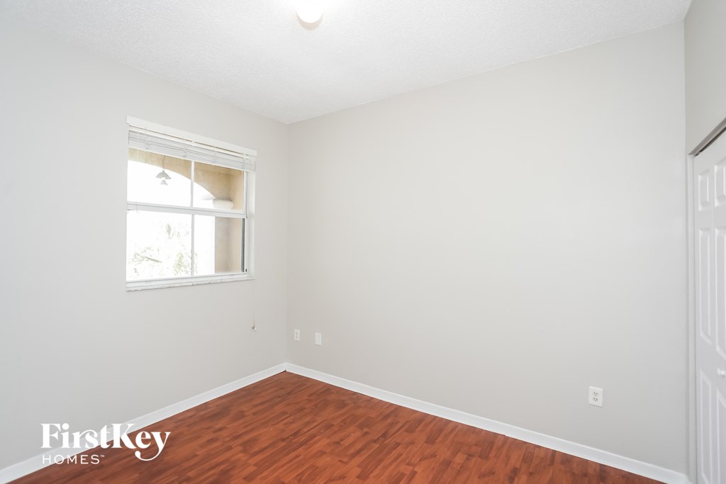 a bedroom with white walls and wood flooring and a window