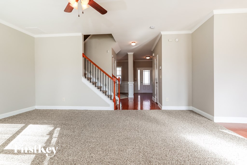 an empty living room with a ceiling fan and a hallway with stairs