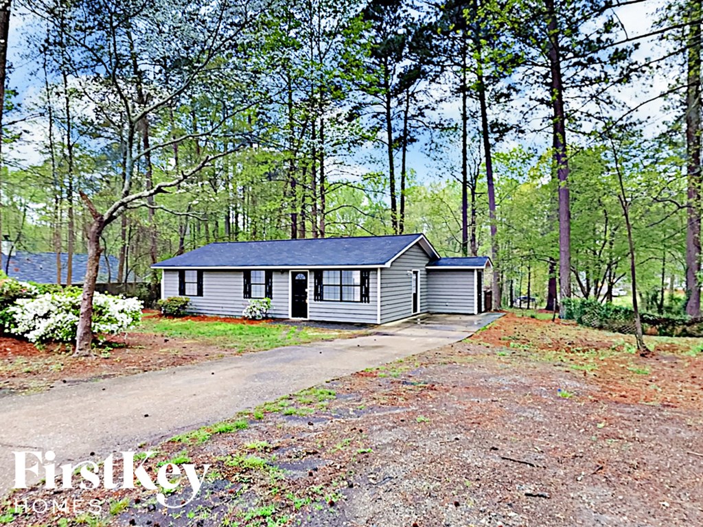 A house is surrounded by trees and has a gravel driveway.