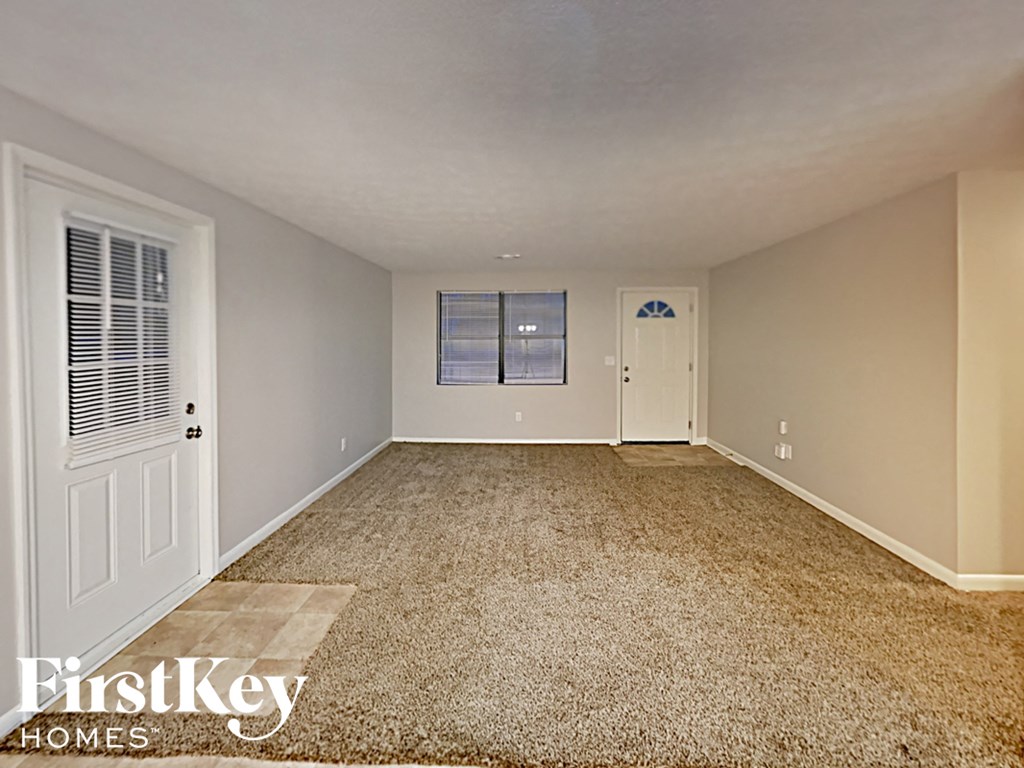 A carpeted room with a window and a door.