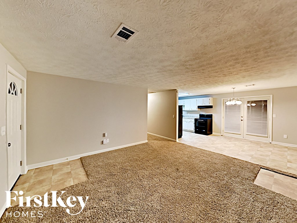 A spacious room with a carpeted floor and a door on the left side.