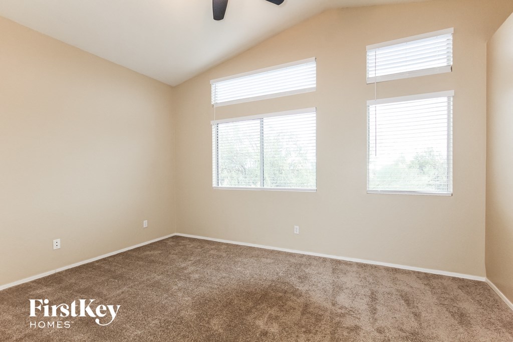 a carpeted room with three windows and a ceiling fan