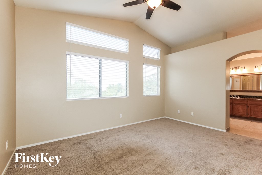 an empty living room with a ceiling fan and three windows