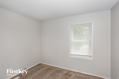 A room with a carpeted floor and a window with blinds.