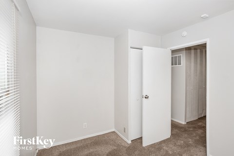 A white bedroom with a carpeted floor and a closet with a door open.