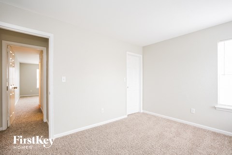 a bedroom with white walls and carpet and a door to a hallway