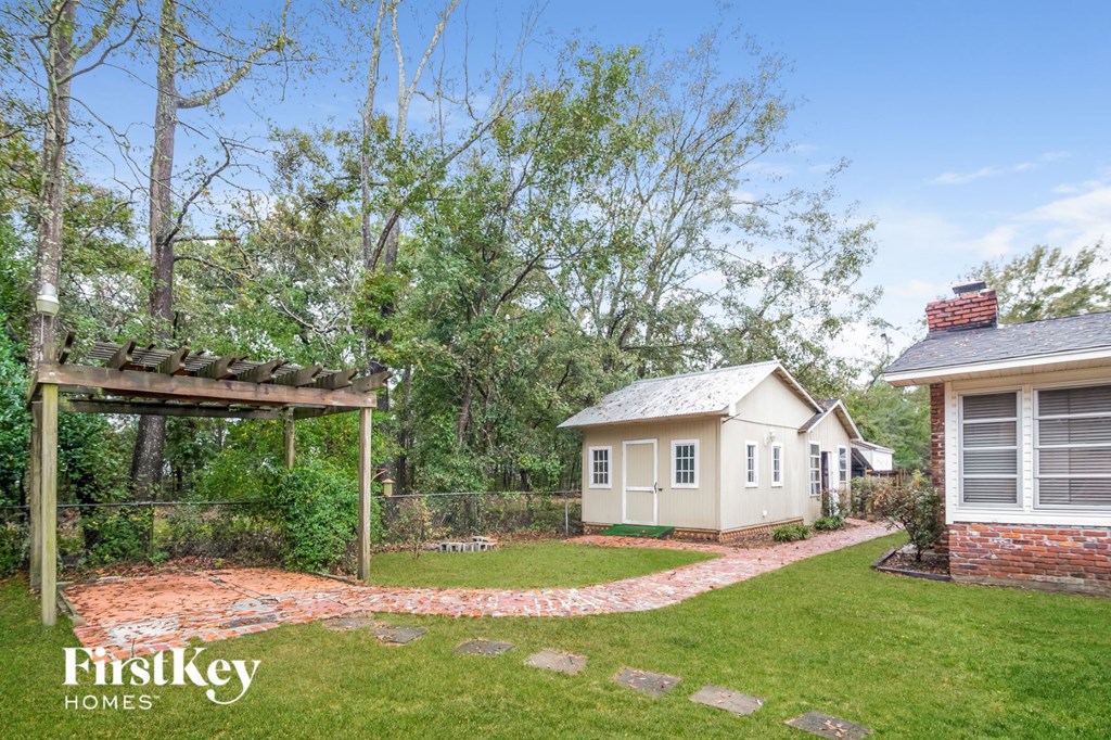 A small house is surrounded by a garden and a wooden pergola.