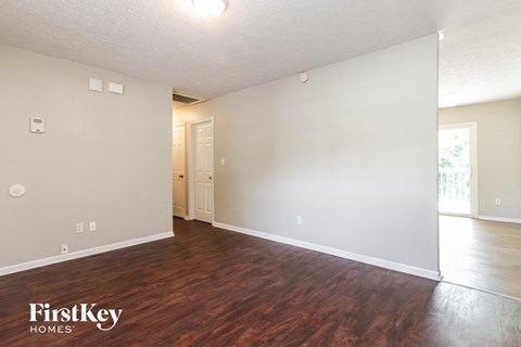 A room with wooden floors and white walls, with a door leading to another room.