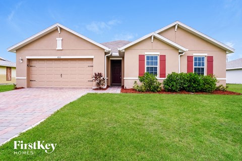 a beige house with red shutters and a lawn