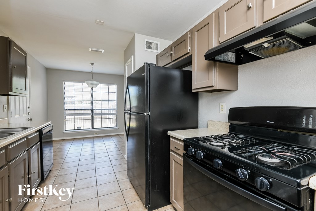 A black refrigerator in a kitchen with a stove and cabinets.