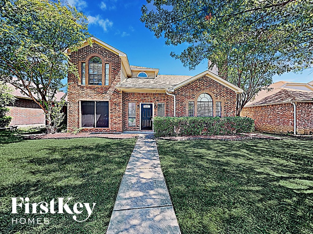A brick house with a large front yard and a sidewalk leading to the front door.
