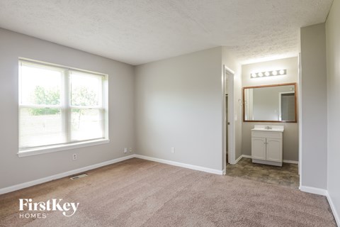 A bedroom with a carpeted floor and a small bathroom with a mirror and sink.