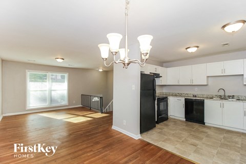 A well-lit kitchen and living room with a chandelier and a view of the outdoors through the windows.