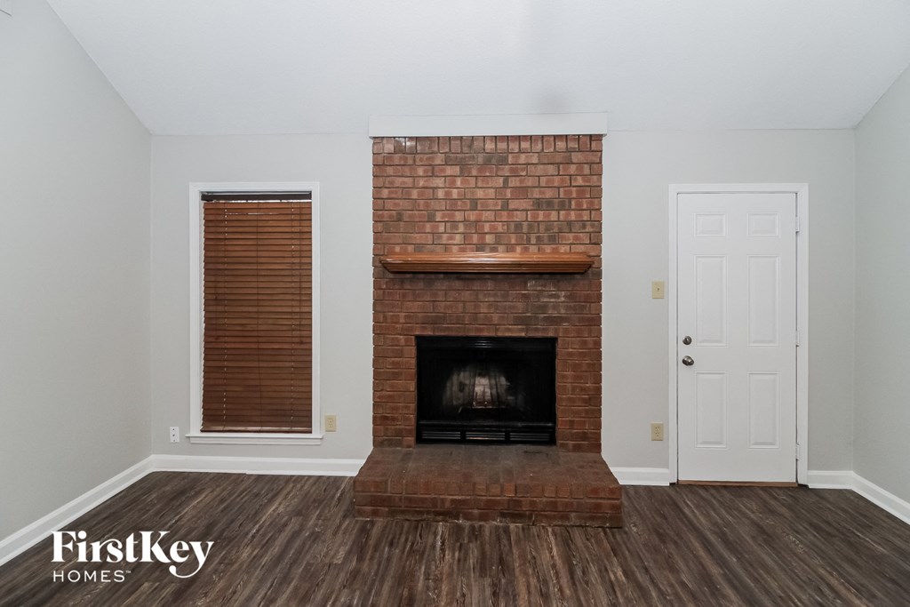 the living room of a home with a brick fireplace and wooden floors