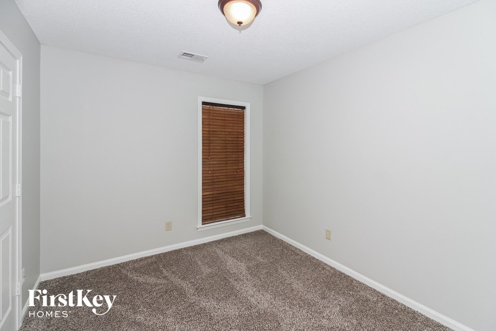 a bedroom with white walls and carpet and a window with a wooden door