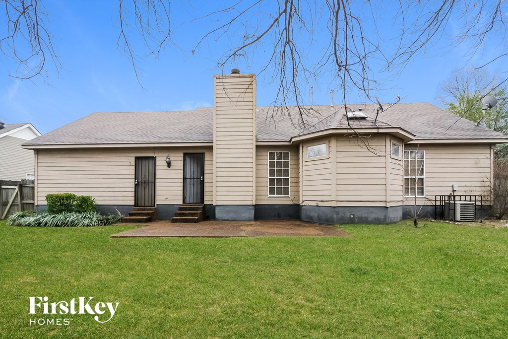 the front of a tan house with a yard and a backdoor
