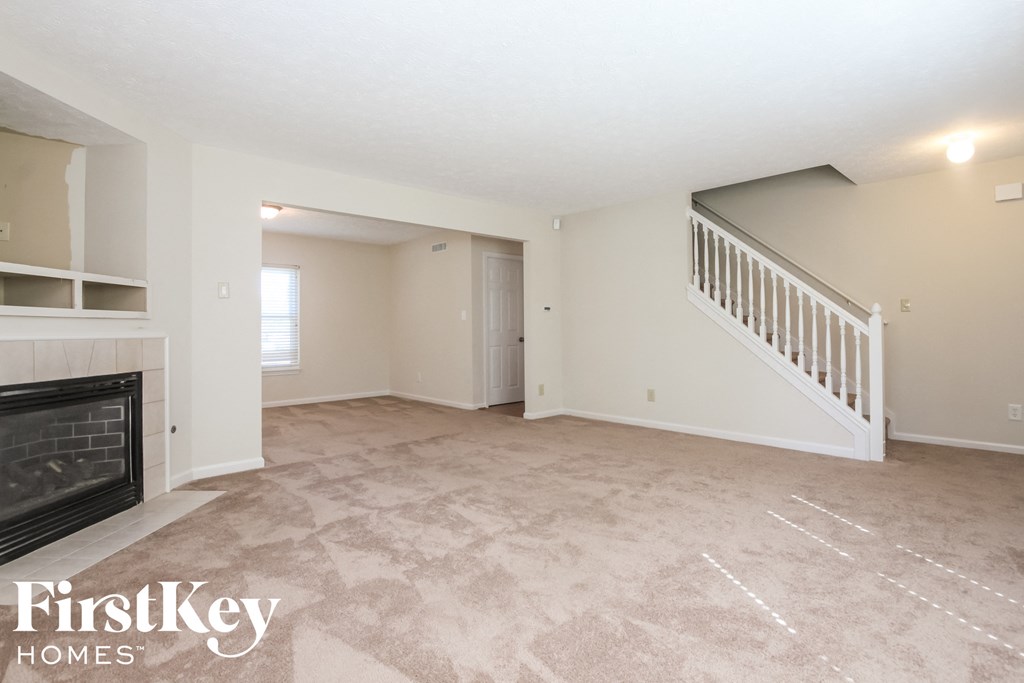 A spacious living room with a fireplace and a staircase.