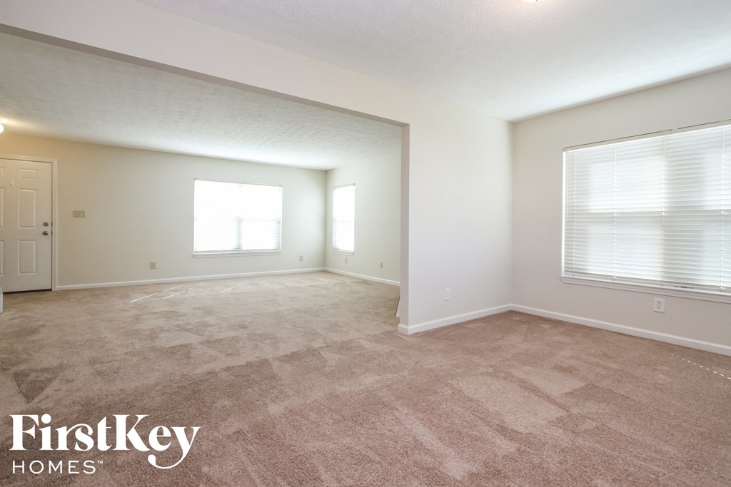 A spacious room with a carpeted floor and a window with blinds.