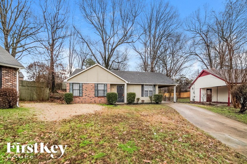 A house with a red roof is situated in a grassy area with a driveway leading to the front door.