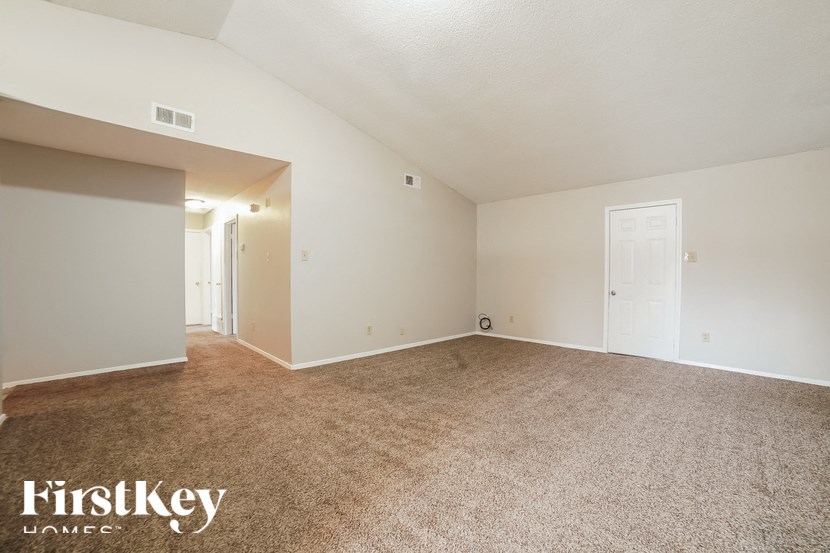 A spacious room with a carpeted floor and white walls, with a door on the right side.