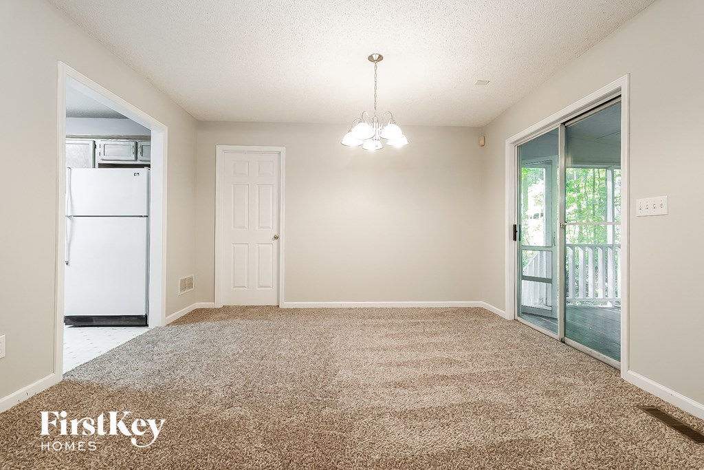 an empty living room with a white refrigerator and a door to a balcony